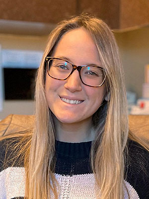 White woman with long blonde hair wearing glasses and a striped black and white sweater