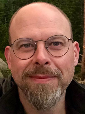 White man with light brown and grey goatee wearing round glasses